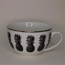 A wide rounded cup with a handle facing right 
                            A white cup with a print of black pineapples and a golden rim 
                            An empty cup in studio