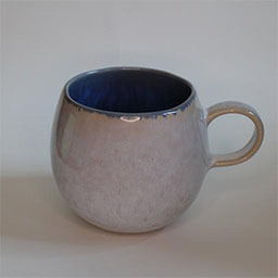 A uneven round cup with a handle facing right 
                            A greyish white stone cup blue on the inside 
                            An empty cup in studio