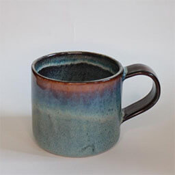 A uneven cylindric cup with a handle facing right 
                            A gradient blue green brown stone cup with a white line 
                            An empty cup in studio