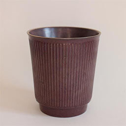 A cone shaped cup without a handle 
                            A dark brown stone cup with vertical grooves 
                            An empty cup in studio