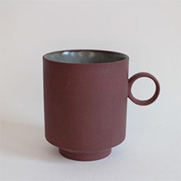 A cylindric cup with a round handle facing right 
                            A red brown cup olive on the inside 
                            An empty cup in studio
