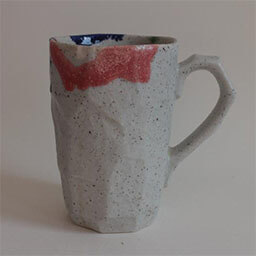 A high cone shaped cup with a handle facing right 
                            A geometric grey stone cup with red blue and green splashes of color 
                            An empty cup in studio