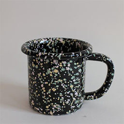 A cylindric camping cup with a handle facing right 
                            A black cup sprinkled with yellow green and rose splashes of color 
                            An empty cup in studio