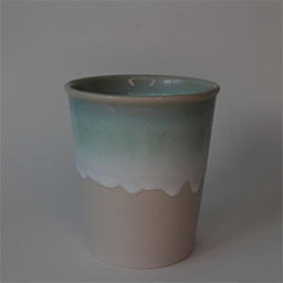 A cone shaped cup without a handle 
                            A grey stone cup half glazed with white and turquoise 
                            An empty cup in studio