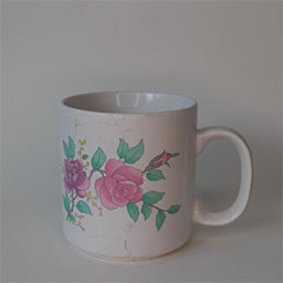 A cylindric cup with a handle facing right 
                            A white cup printed with green and pink flower illustrations 
                            An empty cup in studio