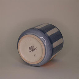 a cylindric cup lying on its side facing back a blue and white striped cup painted with an orange illustration an empty cup in studio